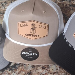 May include: Three trucker hats with the text "LONG LIVE COWBOYS" on a leather patch. The hats have different color combinations: gray with a black mesh, tan with a white mesh, and gray with a black brim.