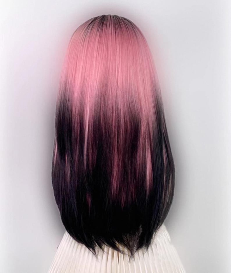 May include: A long, straight wig with a pink to black ombre colour gradient. The wig is styled with a centre parting and falls to the shoulders.