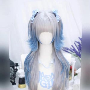 Puede incluir: Una peluca larga, lisa, plateada con reflejos azules. La peluca tiene raya lateral y flequillo. La peluca está peinada en dos coletas con cintas azules.