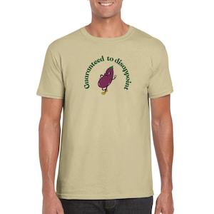 May include: A beige t-shirt with a cartoon eggplant character. The eggplant is purple with yellow shoes and arms. Above the eggplant, the text reads "Guaranteed to disappoint" in a green, arched font. The t-shirt is short-sleeved.