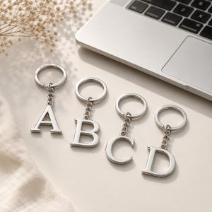 May include: Four silver-toned metal keychains featuring the capital letters A, B, C, and D. Each keychain consists of a circular split ring attached to a short chain that connects to a polished, serif-style letter charm with a smooth finish.