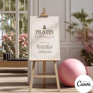 Könnte beinhalten: Ein Holzstaffelei mit einem Pilates-Geburtstagsschild. Das Schild hat einen gestreiften Hintergrund mit dem Text "Pilates with the birthday girl" und "Amanda's 21st Birthday". Ein rosa Gymnastikball befindet sich daneben.