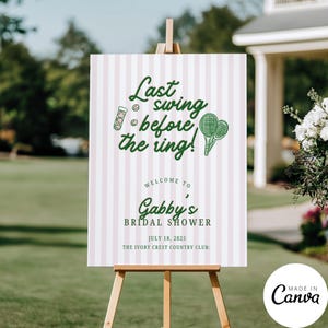 May include: A sign on a wooden easel with the text "Last swing before the ring!" in green script. The sign is for Gabby's bridal shower, with the date July 18, 2025, and the location, The Ivory Crest Country Club. The background has pink and white stripes.