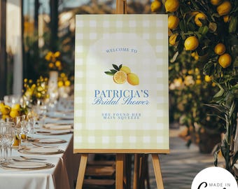 May include: A sign on a wooden easel, welcoming guests to Patricia's bridal shower. The sign features a light green and white gingham pattern, with the words "Welcome to" and "Patricia's Bridal Shower" in blue script. Lemon illustrations and the phrase "She found her main squeeze" are also included.