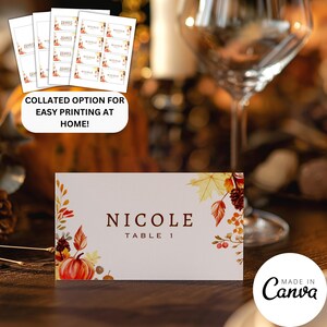 May include: A printable place card with a fall theme. The card features a watercolor illustration of pumpkins, leaves, and berries. The text "NICOLE TABLE 1" is printed in brown on the card.