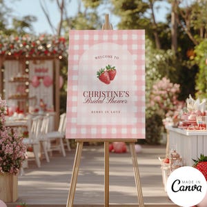 May include: A pink and white gingham welcome sign on a wooden easel. The sign reads "Welcome to Christine's Bridal Shower" with strawberry illustrations and the phrase "Berry in Love."