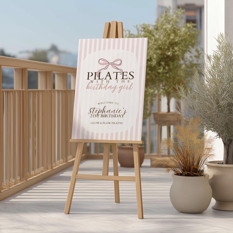 Peut inclure: Un chevalet en bois supportant une affiche avec le texte "Pilates with the birthday girl". L'affiche pr&eacute;sente un fond &agrave; rayures roses et blanches et un motif de n&oelig;ud. Elle souhaite la bienvenue &agrave; l'anniversaire de St&eacute;phanie.