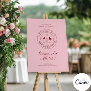 May include: Pink welcome sign with a red circle logo that says "Alexandra's Bridal Shower" with a graphic of two paddle rackets and hearts. The sign also says "Welcome to the Grand Slam Event", "Game, Set, Match!" and "July 18, 2025 The Ivory Crest Country Club".
