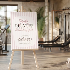 Peut inclure: Panneau de bienvenue sur chevalet en bois, avec un design &agrave; rayures roses et blanches. Le panneau indique "Pilates avec la fille d'anniversaire" et souhaite la bienvenue aux invit&eacute;s &agrave; l'anniversaire de Stephanie, 21 ans, chez Glow & Flow Pilates.