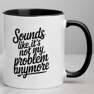 Könnte beinhalten: Weiße Keramik-Kaffeetasse mit schwarzem Rand und Henkel. Die Tasse hat einen schwarzen Schriftzug mit der Aufschrift "Sounds like it's not my problem anymore".
