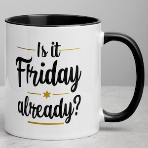 Può includere: Tazza da caffè in ceramica bianca con bordo e manico neri. La tazza ha testo nero che recita "Is it Friday already?" con una stella dorata e linee sopra e sotto il testo.