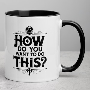 Könnte beinhalten: Weißer Keramikbecher mit schwarzem Innenraum und Henkel. Der Becher zeigt den Text "HOW DO YOU WANT TO DO THIS?" in Schwarz, mit dekorativen Elementen. Das Design beinhaltet eine geometrische Form oben, was auf ein Gaming-Thema hindeutet.