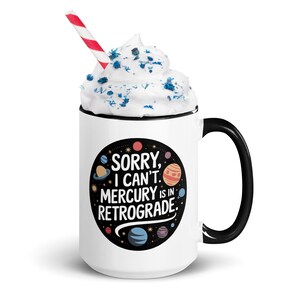 Peut inclure: Une tasse en c&eacute;ramique blanche avec une anse et un bord noirs. La tasse pr&eacute;sente un cercle noir avec des plan&egrave;tes color&eacute;es et le texte "D&eacute;sol&eacute;, je ne peux pas. Mercure est en r&eacute;trograde."