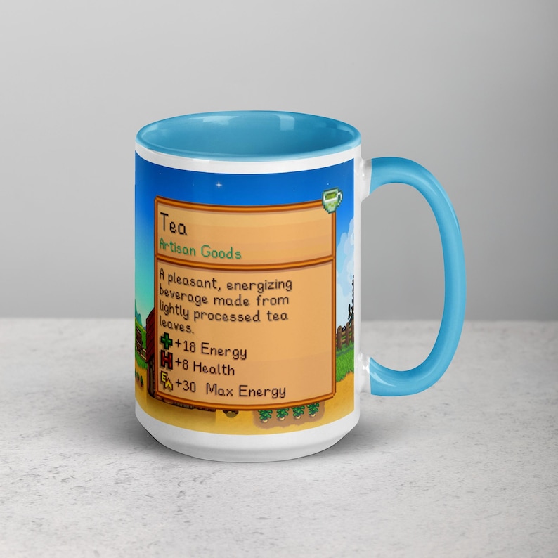 May include: A white ceramic mug with a blue interior and handle. The mug features a colorful graphic with the word "Tea" and text describing an energizing beverage made from tea leaves. The mug is a standard 11 oz size.