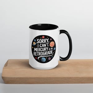 Peut inclure: Une tasse en c&eacute;ramique blanche avec un bord et une poign&eacute;e noirs. La tasse pr&eacute;sente un motif noir et blanc de plan&egrave;tes et d'&eacute;toiles avec le texte "D&eacute;sol&eacute;, je ne peux pas. Mercure est r&eacute;trograde."