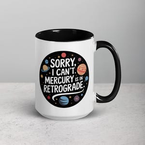 Peut inclure: Une tasse en c&eacute;ramique blanche avec un bord et une poign&eacute;e noirs. La tasse pr&eacute;sente un cercle noir avec un contour blanc et le texte "D&eacute;sol&eacute;, je ne peux pas. Mercure est r&eacute;trograde." en blanc. Le cercle est rempli de plan&egrave;tes et d'&eacute;toiles color&eacute;es.