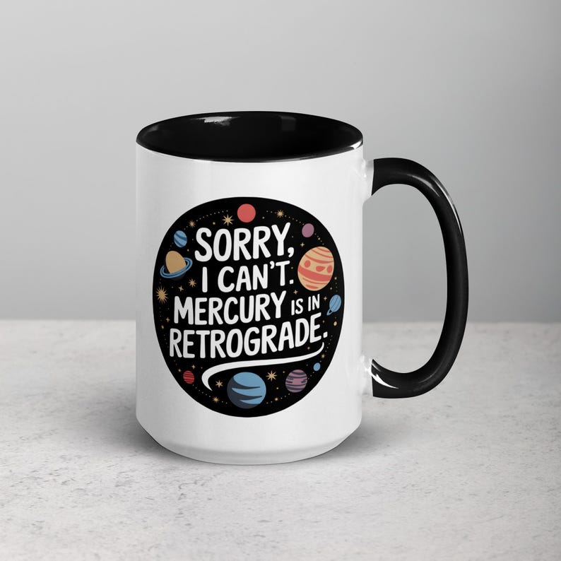 Peut inclure: Une tasse en c&eacute;ramique blanche avec un bord et une poign&eacute;e noirs. La tasse pr&eacute;sente un cercle noir avec un contour blanc et le texte "D&eacute;sol&eacute;, je ne peux pas. Mercure est r&eacute;trograde." en blanc. Le cercle est rempli de plan&egrave;tes et d'&eacute;toiles color&eacute;es.