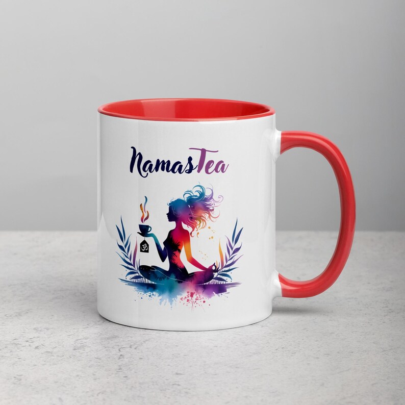 K&ouml;nnte beinhalten: Wei&szlig;e Keramiktasse mit rotem Rand und Henkel. Die Tasse zeigt eine farbenfrohe Illustration einer Frau in einer Yoga-Pose, die eine Tasse Tee h&auml;lt. Der Text "Namastea" ist in Schwarz auf die Tasse gedruckt.
