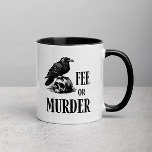 May include: White ceramic mug with a black interior and handle. The mug features a black and white illustration of a raven perched on a skull, with the words "FEE OR MURDER" printed below the skull.