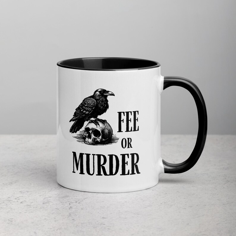 May include: White ceramic mug with a black interior and handle. The mug features a black and white illustration of a raven perched on a skull, with the words "FEE OR MURDER" printed below the skull.