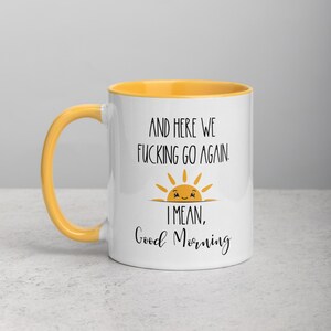 Pu&ograve; includere: Tazza in ceramica bianca con bordo giallo. La tazza ha un motivo nero di un sole sorridente con il testo "And here we fucking go again. I mean, Good Morning".