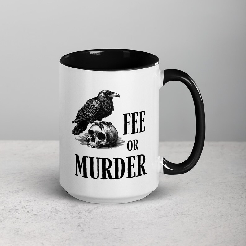 May include: White ceramic mug with a black interior and handle. The mug features a black and white illustration of a raven perched on a skull. The text "FEE OR MURDER" is printed below the raven and skull.