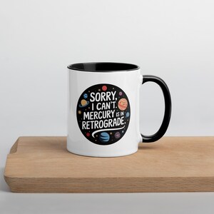 Peut inclure: Une tasse en c&eacute;ramique blanche avec un bord et une poign&eacute;e noirs. La tasse pr&eacute;sente un motif noir et blanc de plan&egrave;tes et le texte "D&eacute;sol&eacute;, je ne peux pas. Mercure est r&eacute;trograde."