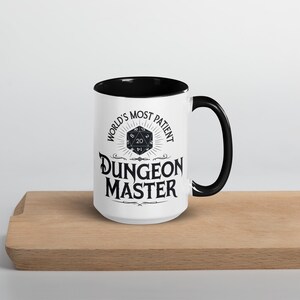 May include: White ceramic mug with a black rim and handle. The mug features a black and white graphic of a twenty-sided die with the text "World's Most Patient Dungeon Master".