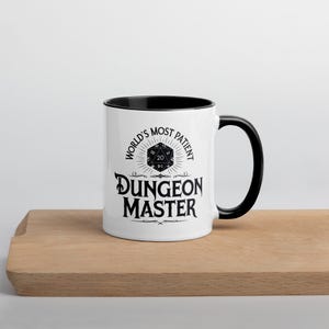 May include: White ceramic mug with a black rim and handle. The mug features a black and white graphic of a twenty-sided die with the text "World's Most Patient Dungeon Master".