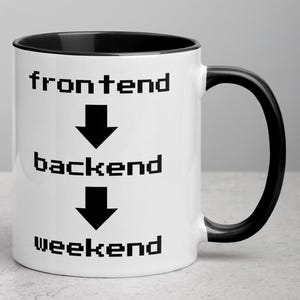 Könnte beinhalten: Weiße Keramik-Kaffeetasse mit schwarzem Rand und Henkel. Die Tasse hat schwarzen Text, der "frontend", "backend" und "weekend" lautet, mit Pfeilen, die zwischen den Wörtern nach unten zeigen.