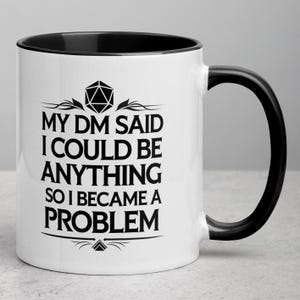 May include: White ceramic mug with a black interior and handle. The mug features the text "MY DM SAID I COULD BE ANYTHING SO I BECAME A PROBLEM" in black, along with a D20 die graphic. A fun gift for tabletop gamers.