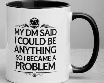 May include: White ceramic mug with a black interior and handle. The mug features the text "MY DM SAID I COULD BE ANYTHING SO I BECAME A PROBLEM" in black, along with a D20 die graphic. A fun gift for tabletop gamers.