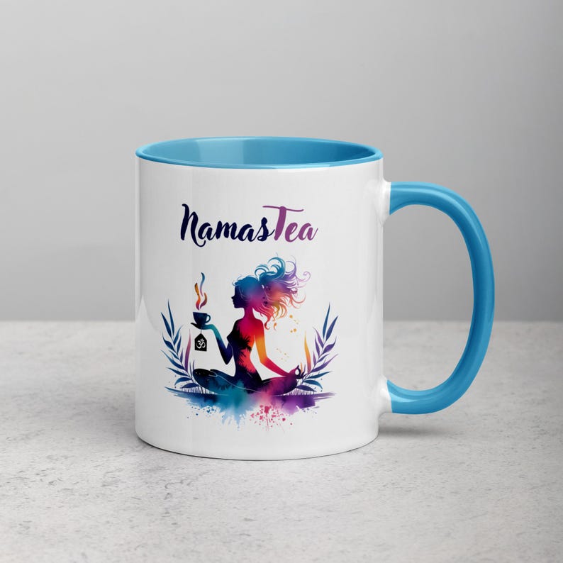 K&ouml;nnte beinhalten: Wei&szlig;e Keramiktasse mit hellblauem Rand und Henkel. Die Tasse zeigt eine farbenfrohe Illustration einer Frau in einer Yoga-Pose, die eine Tasse Tee h&auml;lt. Der Text "Namastea" ist in Schwarz auf die Tasse gedruckt.
