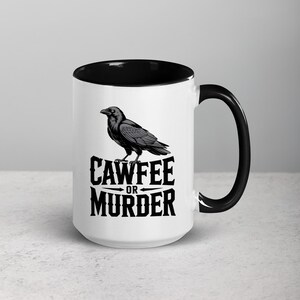May include: White ceramic coffee mug with a black interior and handle. The mug features a black and gray illustration of a raven perched above the words "CAWFEE OR MURDER" in a bold, stylized font. A humorous gift.