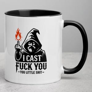 Puede incluir: Taza de cerámica blanca con interior y asa negros. La taza presenta una ilustración en blanco y negro de un mago haciendo la peineta, con el texto "I CAST FUCK YOU - YOU LITTLE SHIT -" en negrita, en negro.