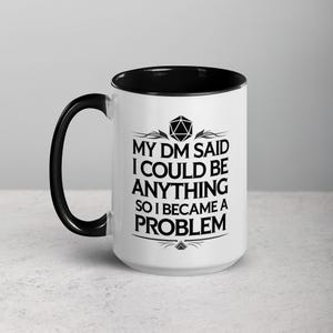May include: White ceramic mug with a black interior and handle. The mug features the text "MY DM SAID I COULD BE ANYTHING SO I BECAME A PROBLEM" in black, along with a geometric design. The mug is designed for fans of tabletop role-playing games.