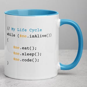 Può includere: Una tazza in ceramica bianca con un bordo e un manico di colore blu chiaro. La tazza presenta un codice umoristico che recita "// My Life Cycle while ($me.isAlive()) { $me.eat(); $me.sleep(); $me.code(); }"