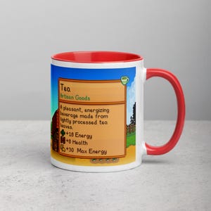 May include: White ceramic mug with a red interior and handle. The mug features a pixelated design with the word "Tea" and game-related text. The design includes a blue sky, brown text box, and green grass.