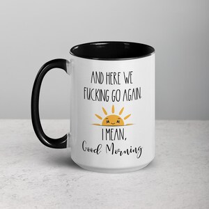 Pu&ograve; includere: Una tazza da caff&egrave; bianca con un bordo nero. La tazza ha un motivo di sole nero e giallo con un viso sorridente e il testo "And here we fucking go again. I mean, Good Morning".