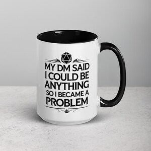 May include: White ceramic mug with a black interior and handle. The mug features the text "MY DM SAID I COULD BE ANYTHING SO I BECAME A PROBLEM" in black, along with a geometric design. A fun gift for a Dungeons and Dragons player.
