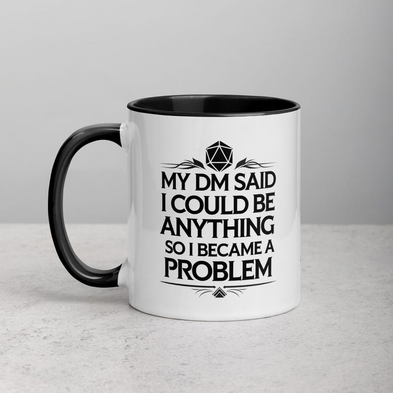 May include: White ceramic mug with a black interior and handle. The mug features the text "MY DM SAID I COULD BE ANYTHING SO I BECAME A PROBLEM" in black, along with a geometric design. A fun gift for a Dungeons and Dragons player.