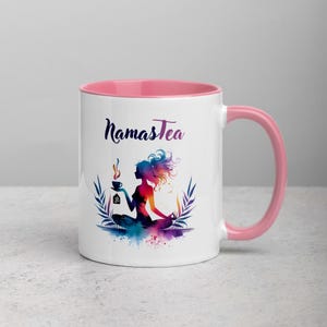K&ouml;nnte beinhalten: Wei&szlig;e Keramiktasse mit rosafarbenem Rand und Henkel. Die Tasse zeigt eine farbenfrohe Illustration einer Frau in einer Yoga-Pose, die eine Tasse Tee h&auml;lt. Der Text "Namastea" ist in Schwarz auf die Tasse gedruckt.
