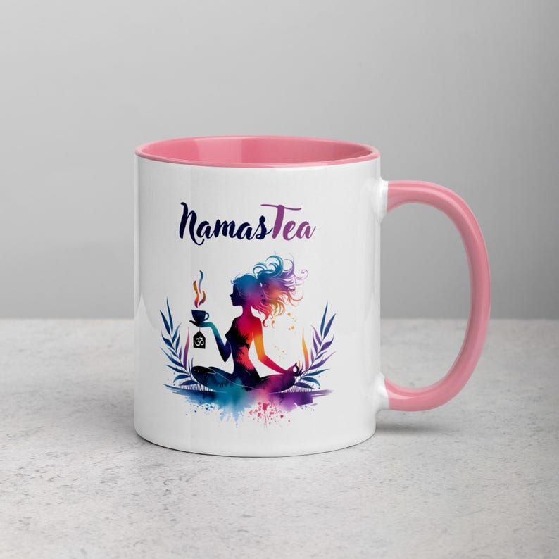 K&ouml;nnte beinhalten: Wei&szlig;e Keramiktasse mit rosafarbenem Rand und Henkel. Die Tasse zeigt eine farbenfrohe Illustration einer Frau in einer Yoga-Pose, die eine Tasse Tee h&auml;lt. Der Text "Namastea" ist in Schwarz auf die Tasse gedruckt.
