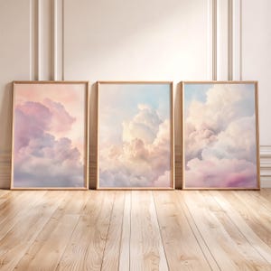 Könnte beinhalten: Drei rechteckige gerahmte Wandbilder mit weichen, ätherischen Wolkenformationen in Pastelltönen wie Rosa, Blau und Creme. Jeder Rahmen besteht aus hellem Holz und zeigt eine durchgehende Himmelsszene mit flauschigen, geschichteten Kumuluswolken.