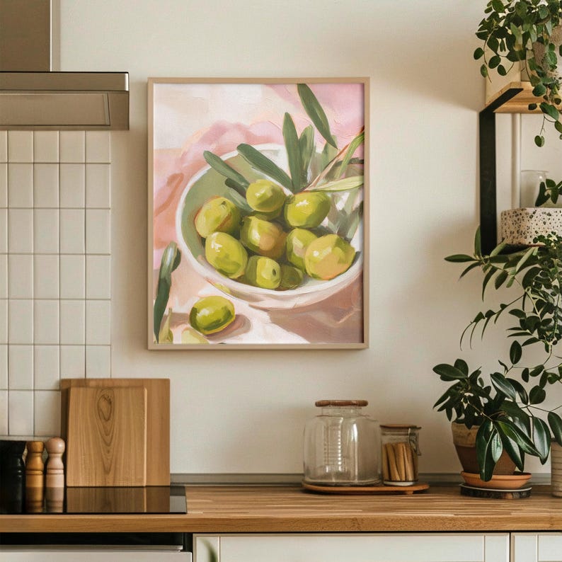 May include: A framed painting of a bowl filled with green olives and olive branches. The bowl is white, and the background features soft pink and white brushstrokes. The artwork is displayed in a kitchen setting.