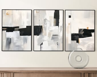 May include: Three abstract paintings in black frames with white, grey, and black geometric shapes. The paintings are hung on a white wall above a wooden dresser.