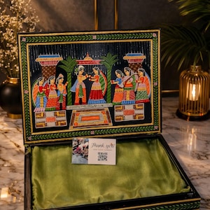 May include: Open wooden box featuring a hand-painted scene of figures in traditional clothing. The box is black with gold trim and a green satin lining. A card inside reads "Thank you".