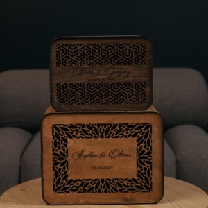 May include: Two rectangular wooden boxes with dark brown finishes. The top box features a geometric pattern and the text Olivia & Gregory MARCH 9, 2029. The bottom box displays a floral-inspired border and the text Sophia & Oliver 03.10.2029.