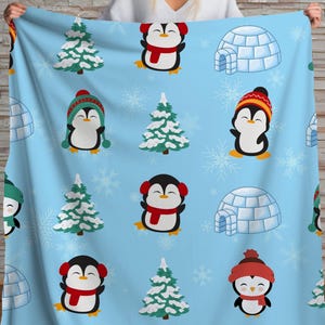 Könnte beinhalten: Hellblaue Decke mit einem sich wiederholenden Muster aus Cartoon-Pinguinen mit Mützen und Schals, schneebedeckten Weihnachtsbäumen und Iglus. Die Pinguine haben Accessoires in verschiedenen Farben, darunter Rot, Grün und Orange. Winterliches Thema.