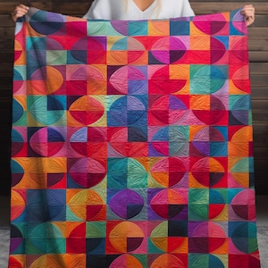 Puede incluir: Una colorida manta con un patrón geométrico de cuadrados y círculos en tonos de rojo, naranja, amarillo, verde, azul y morado. La manta se sostiene, mostrando su vibrante diseño y suave textura. El fondo es una pared de madera.